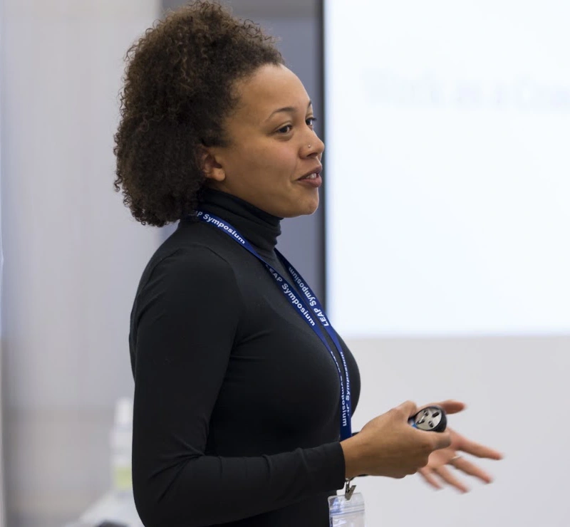 A participant with a Mount Holyoke badge stands at the front of the room