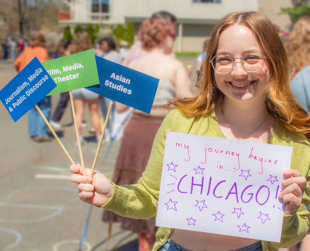 Student holding sign of Journalism, Media & Public Discourse, Film Media, Theater and Asian Studies majors and programs
